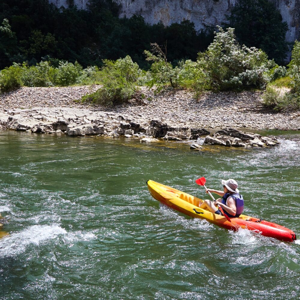 Summer vacation - Back view of young man in a canoe doing kayaking on river. Running the dangerous mountain river in a kayak. Active holidays