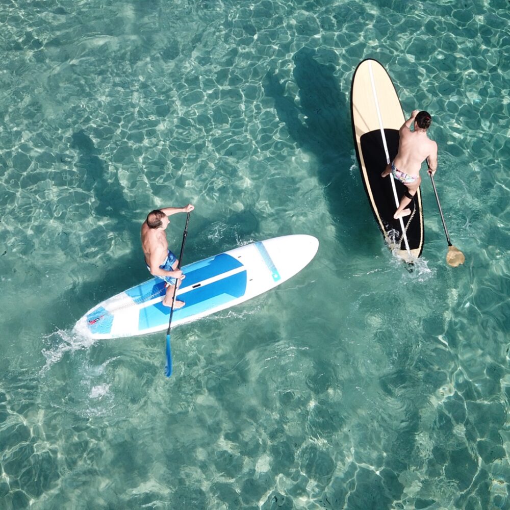 Aerial drone photo of two unidentified men practicing stand up paddle board or SUP in tropical turquoise calm mediterranean beach