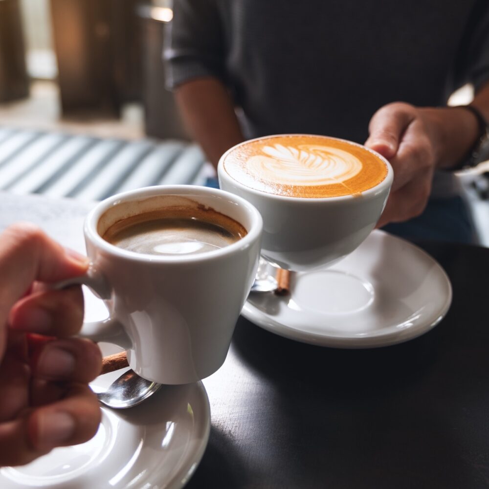Closeup image of a man and a woman clinking white coffee mugs in cafe
